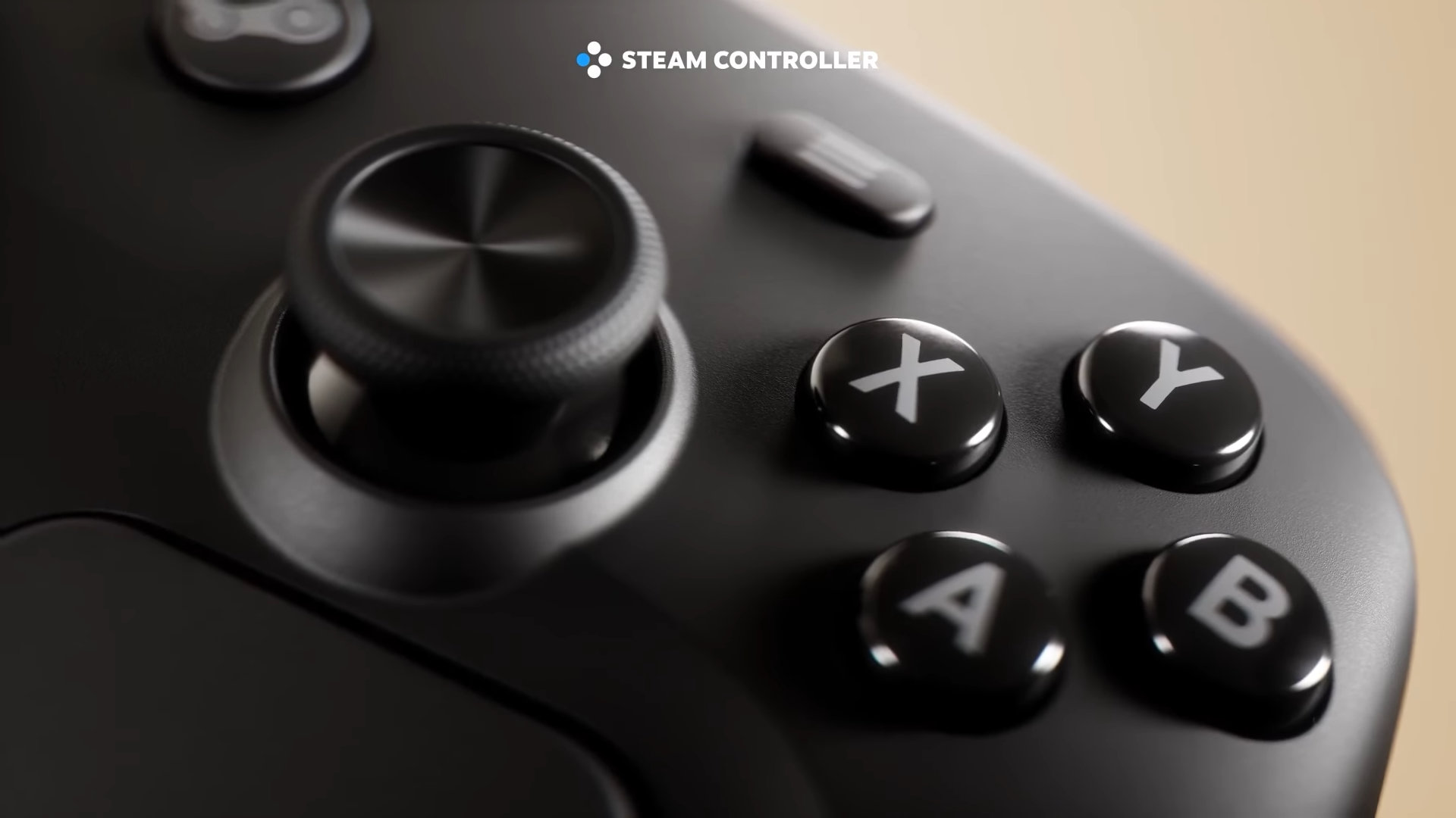 Gros plan détaillé sur une manette Steam Controller de couleur noire, montrant son joystick analogique texturé sur la gauche et les quatre boutons d'action X, Y, A, B brillants sur la droite. Le texte 'STEAM CONTROLLER' est visible en haut à gauche de l'image.