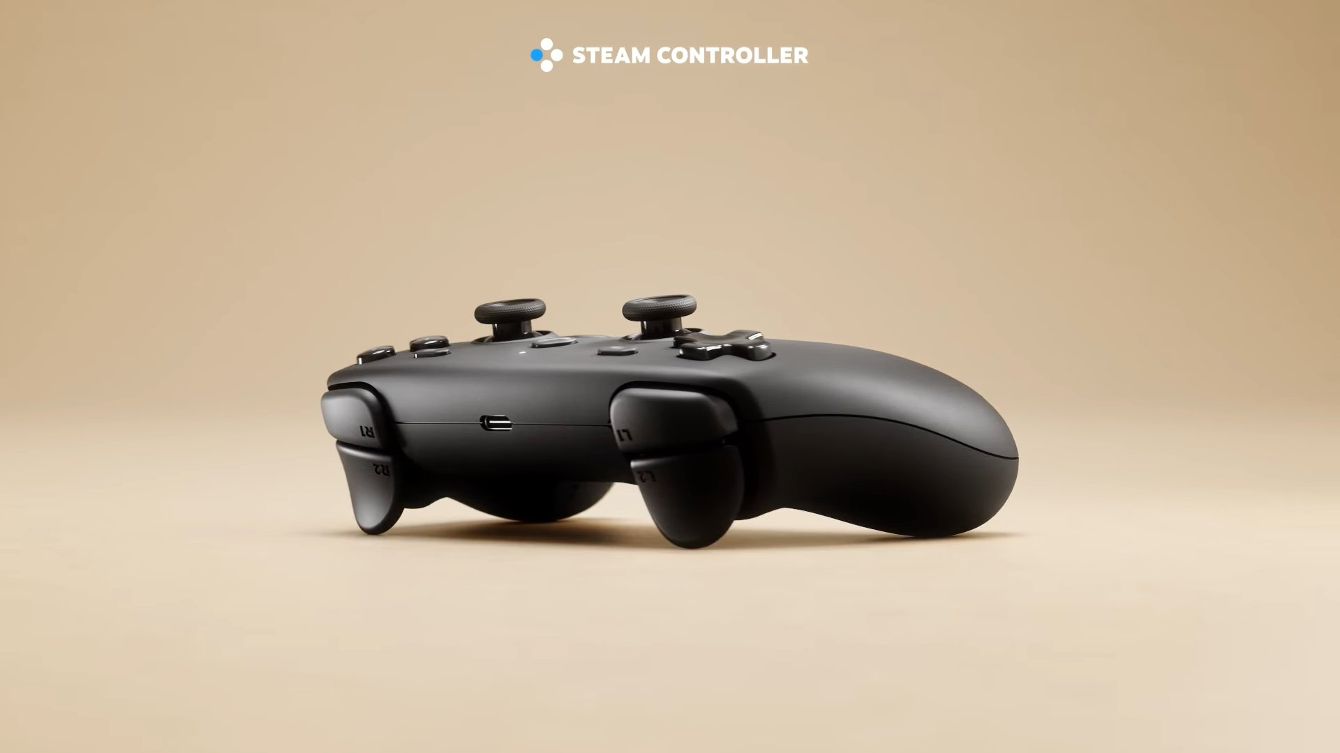 Une manette Steam Controller noire est posée sur une surface beige clair, vue de côté. Les boutons R1, R2, L1, L2, les joysticks et la croix directionnelle sont visibles, ainsi qu'un port USB-C.